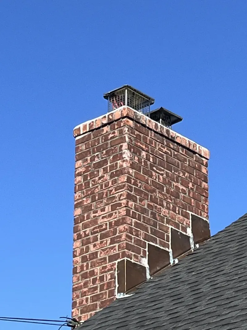 Brick chimney with two stainless steel caps against a blue sky