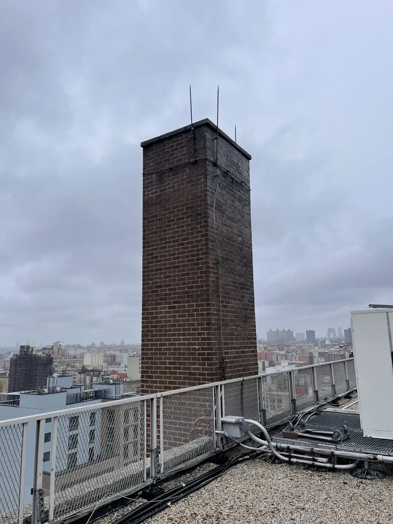Tall brick chimney on a rooftop, with apartment buildings in the distance