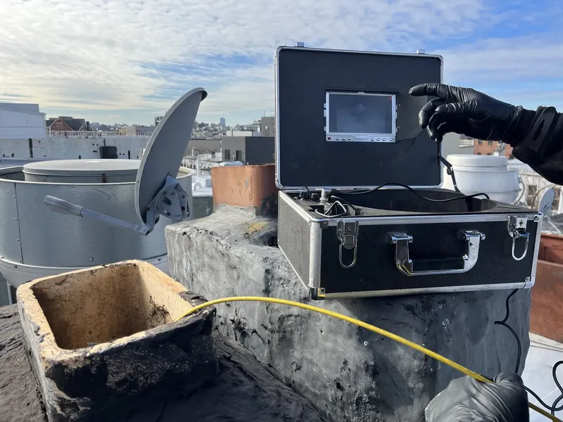 Chimney inspection camera kit open on a rooftop beside a clay flue