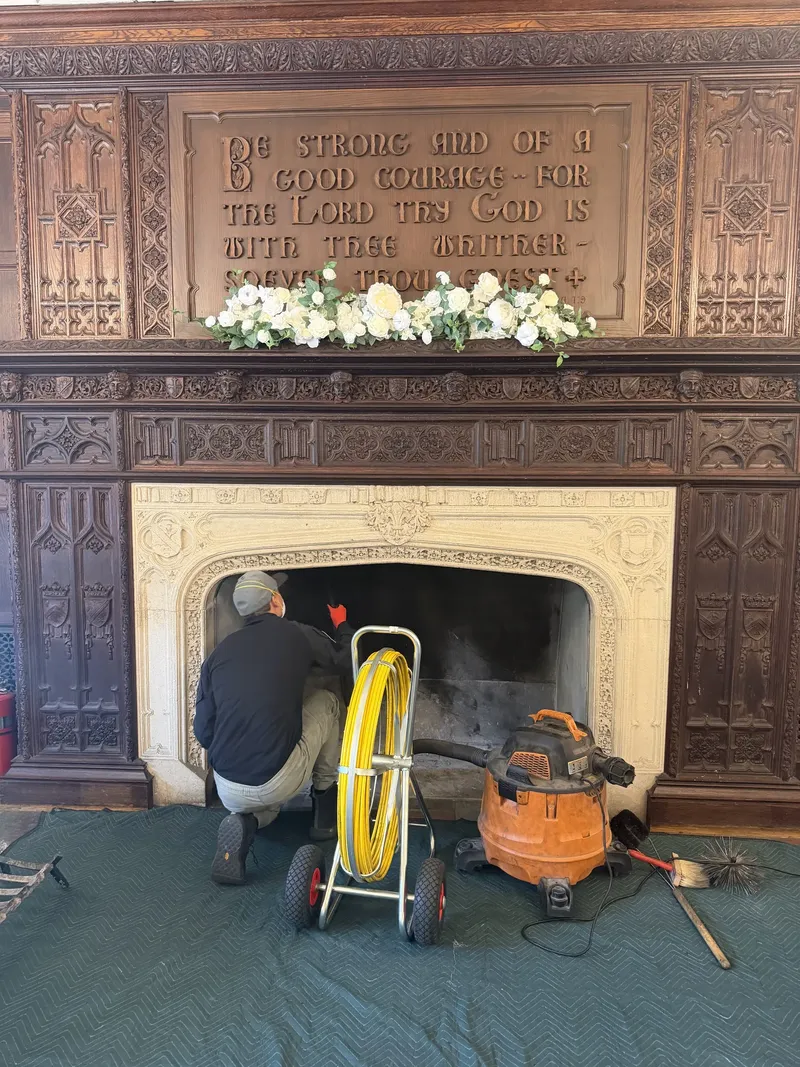 Technician sweeping a carved stone fireplace with a rotary brush and a vacuum, drop cloth on the floor