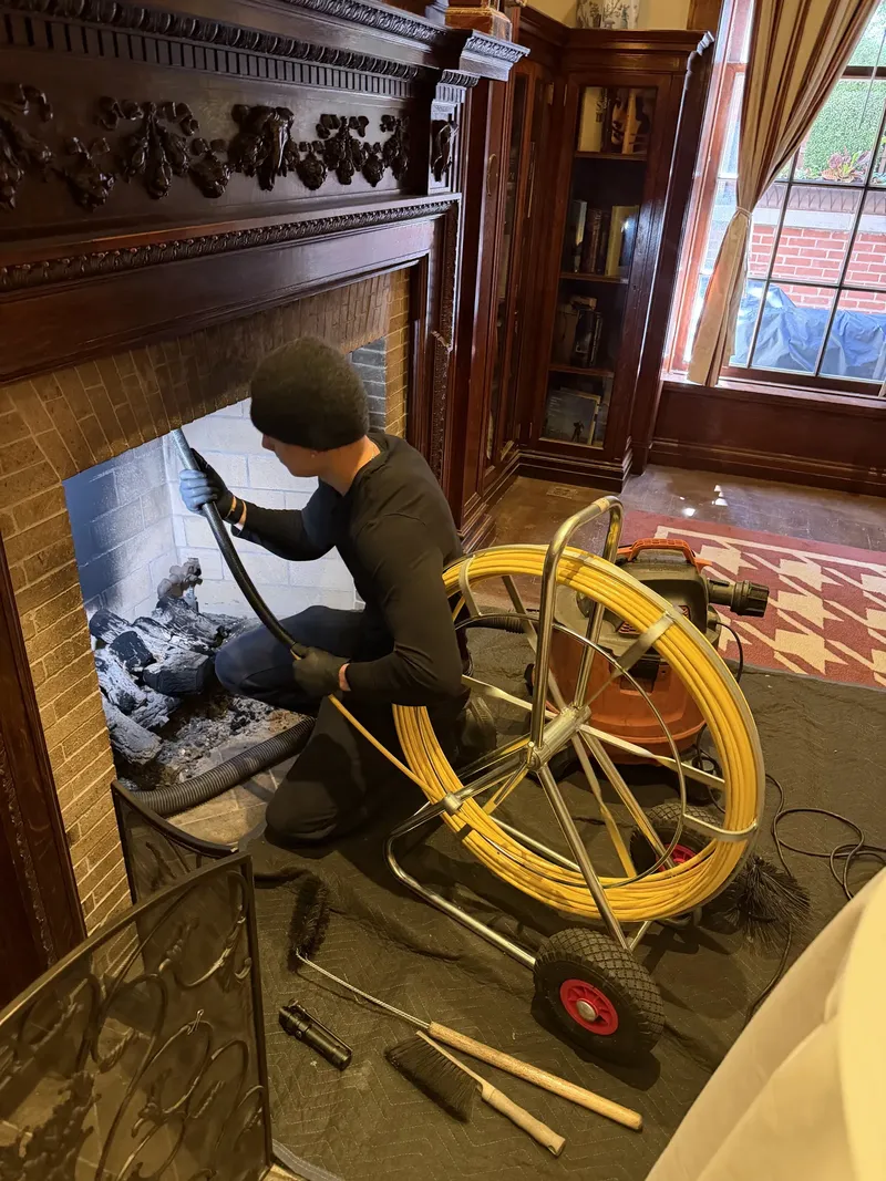 Technician sweeping a dark wood fireplace with a rotary brush reel