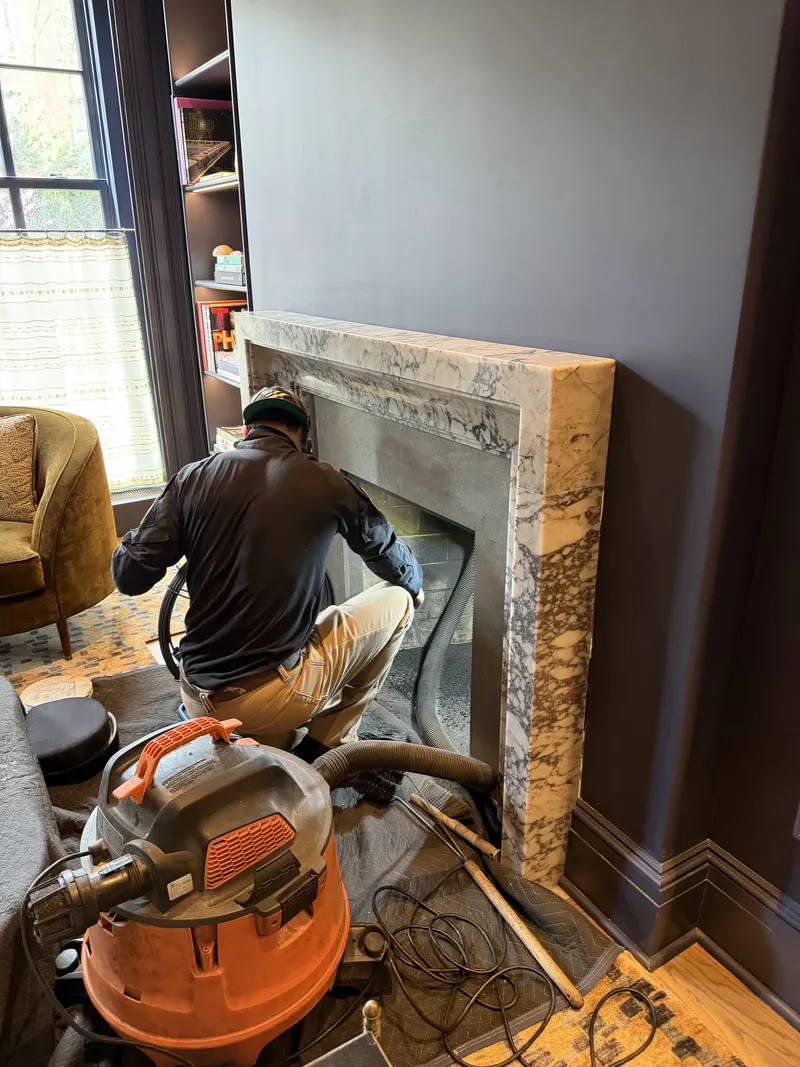 Technician cleaning a marble fireplace with a vacuum, drop cloth on the floor