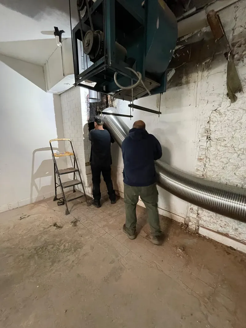 Two technicians installing a stainless steel vent liner in a building basement