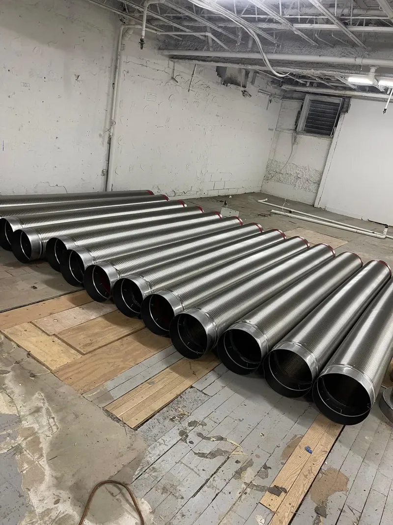 Sections of stainless steel vent pipe laid out on a basement floor