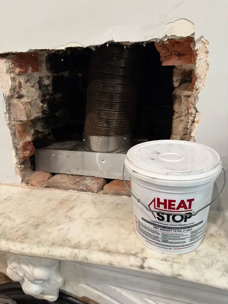 Opened masonry above a fireplace during a repair, with a bucket of heat-resistant mortar