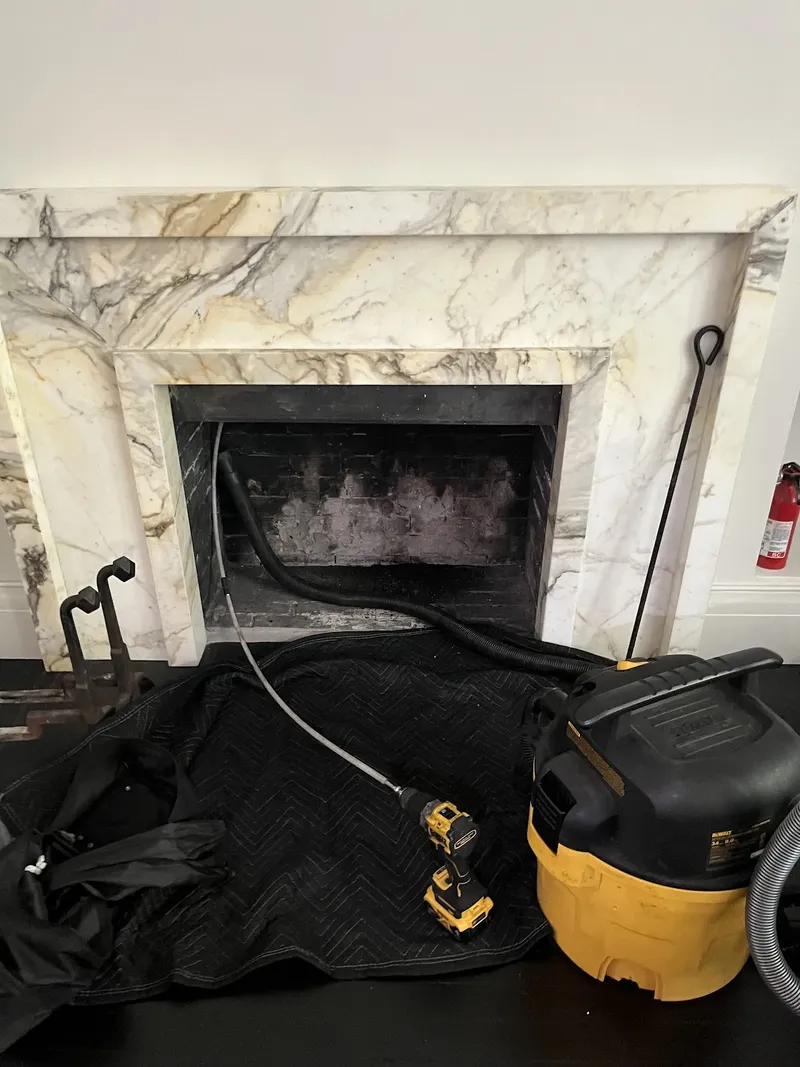 Sweeping a marble fireplace, with a drop cloth on the floor and a vacuum at the opening