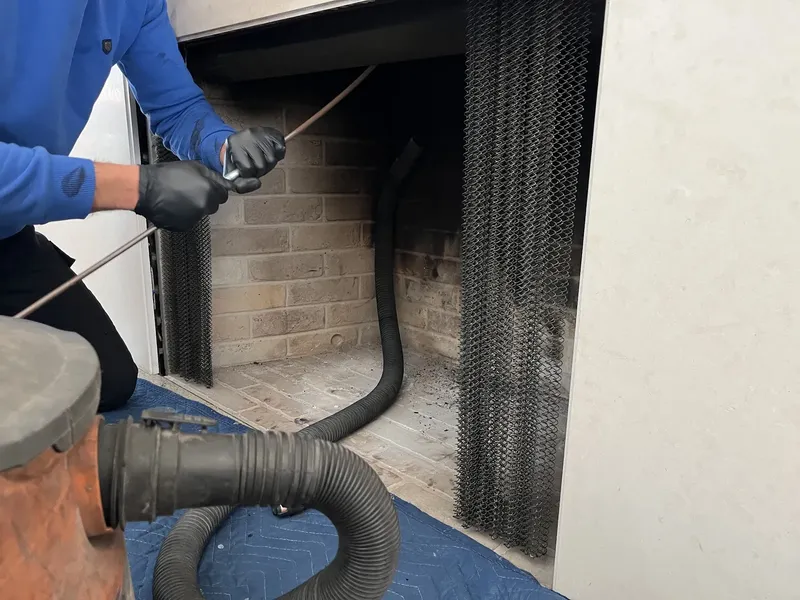 Technician sweeping a fireplace with a vacuum hose, drop cloth on the floor
